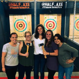 A small group of people posing for picture in an axe throwing bay